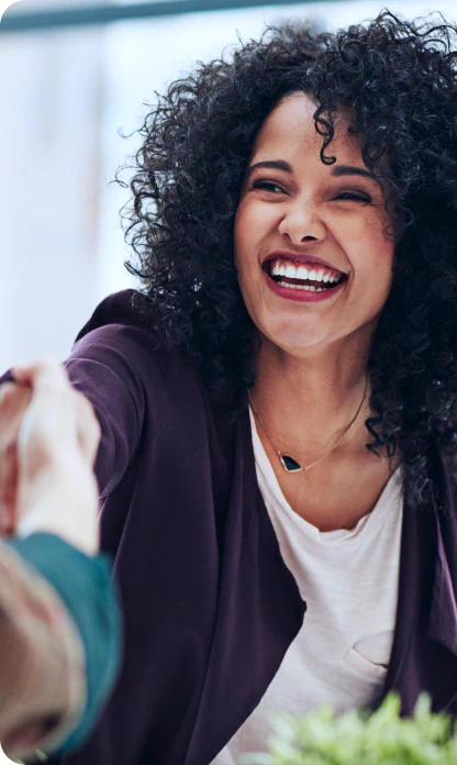 Pessoa vestida como empresária sorrindo e apertando a mão de outra pessoa fechando um acordo